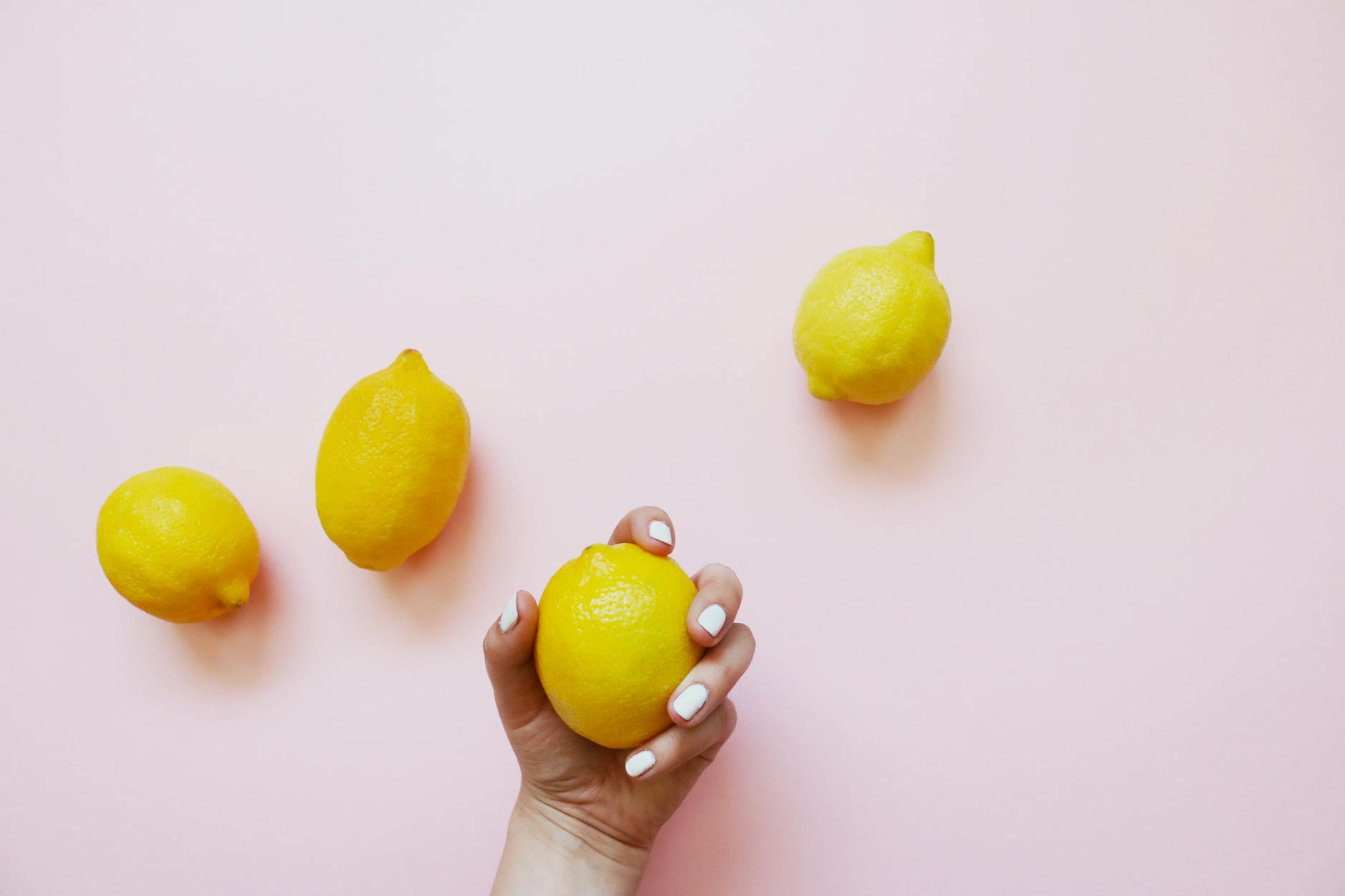 A hand holding a lemon against a soft pink background, symbolizing natural pleasure without performance pressure