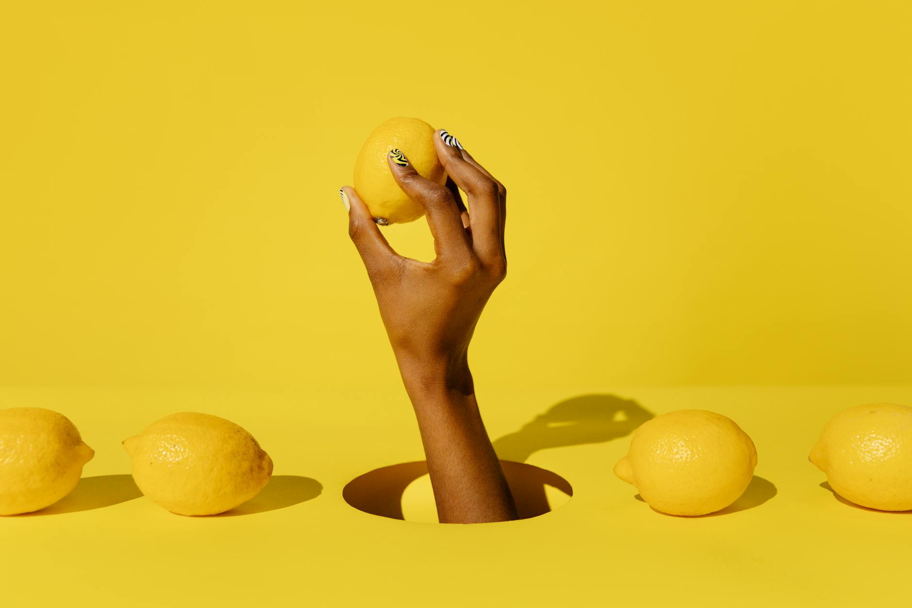 Hand holding a lemon against a vivid yellow background, symbolizing fresh intimacy and natural pleasure