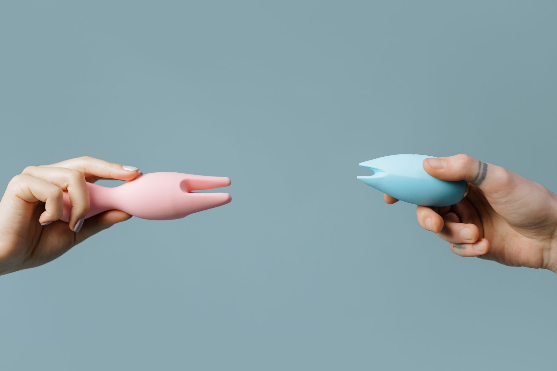 Close-up of hands holding a sleek blue clitoral vibrator against a purple background