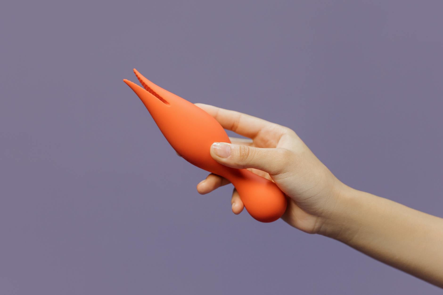 A close-up of a hand holding an orange vibrator against a minimalistic backdrop, representing the gentle return to pleasure.